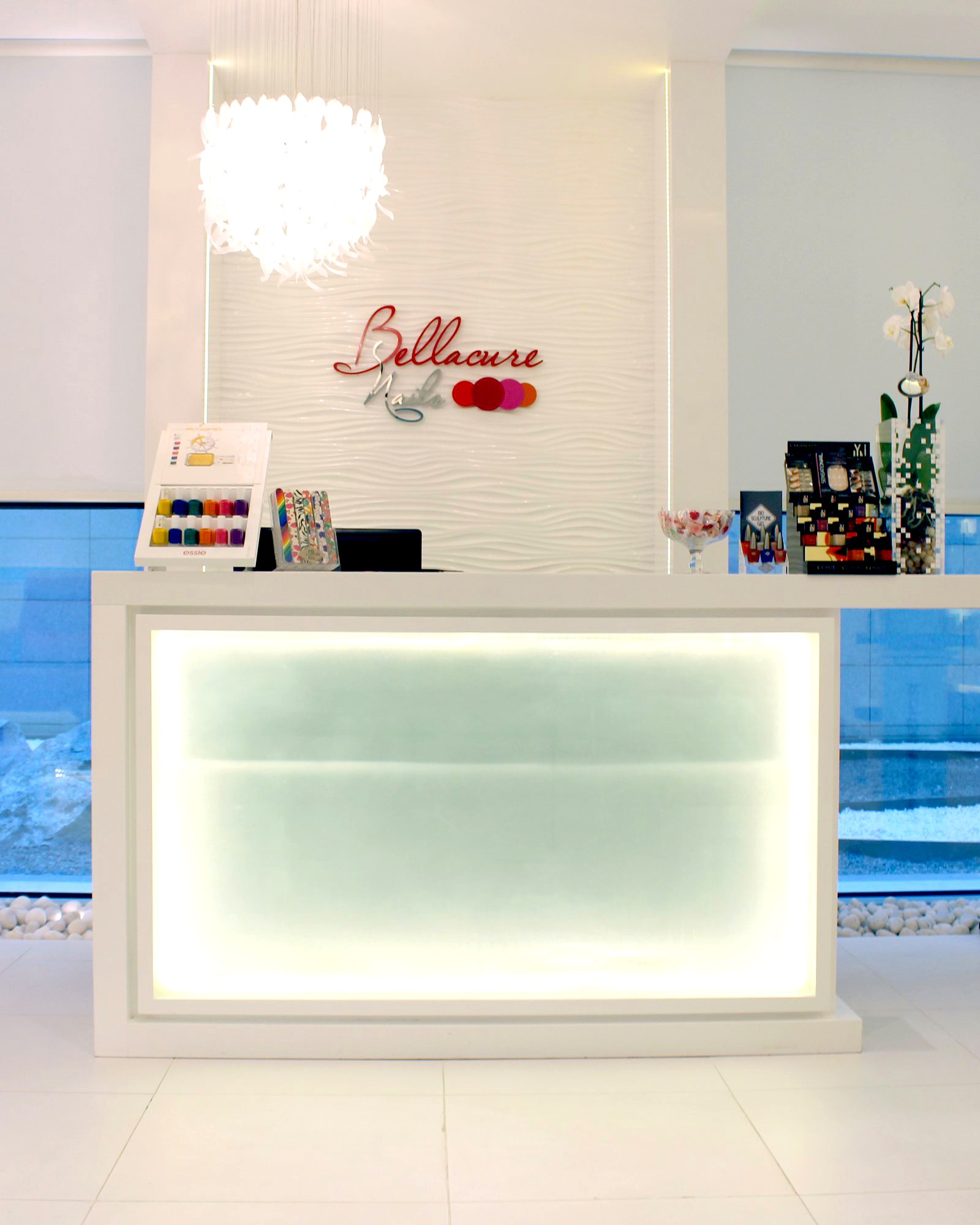 The Bellacure reception at Cleveland Clinic Abu Dhabi: a white desk with a glowing front, nail polish walls and the Bellacure sign