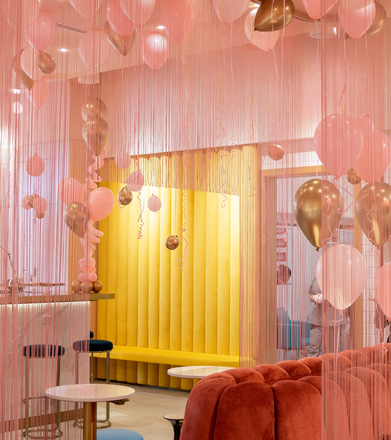 The Bellacure lounge at Al Seef dressed for a party: pink and gold balloons over the yellow banquette, blue chairs and the coral sofa