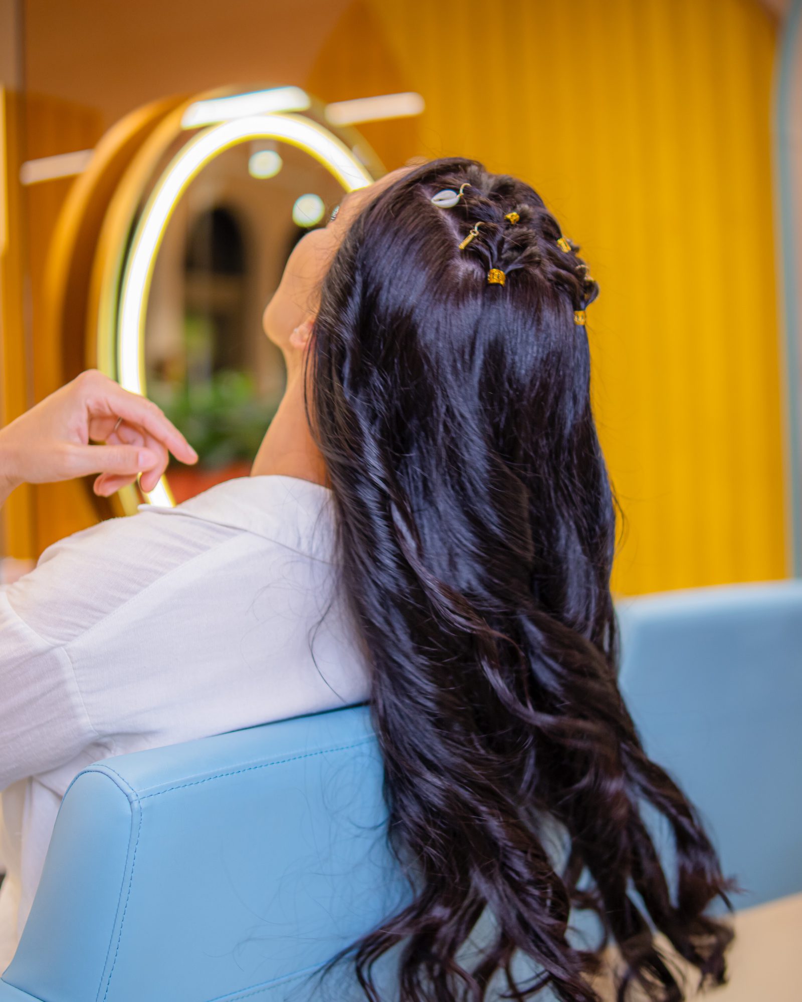Long dark waves with gold hair cuffs, styled in a blue chair under the yellow arches at Bellacure