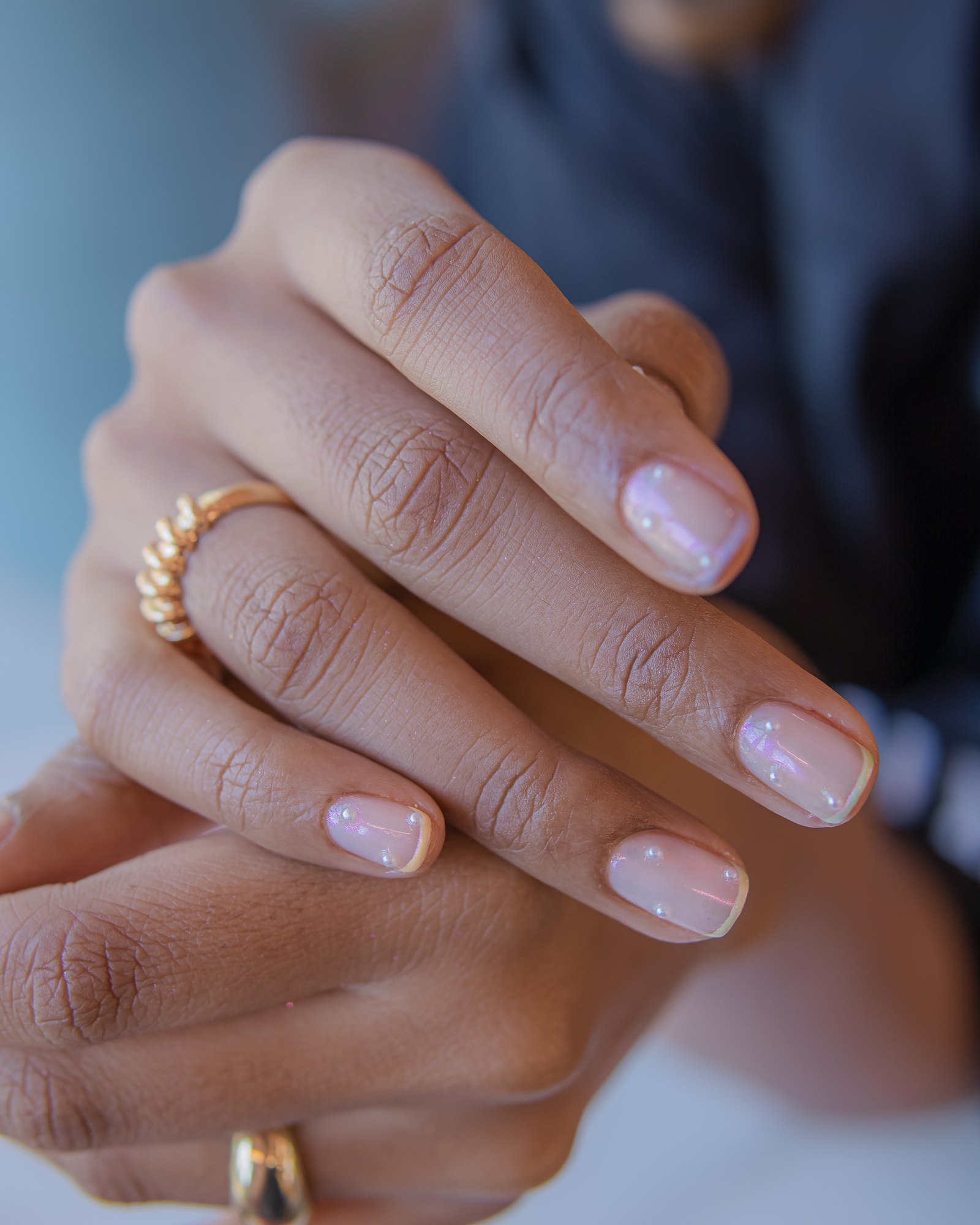 Hands with gold rings and a soft nude manicure at Bellacure