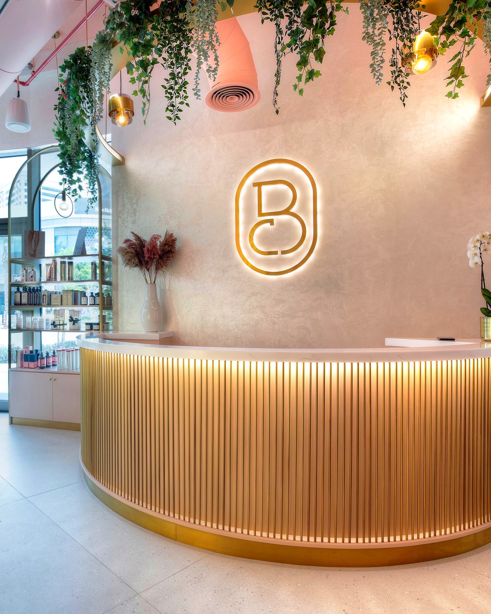 The Sheikha Fatima Park reception: the curved gold desk under trailing plants, with the Bellacure monogram on the wall