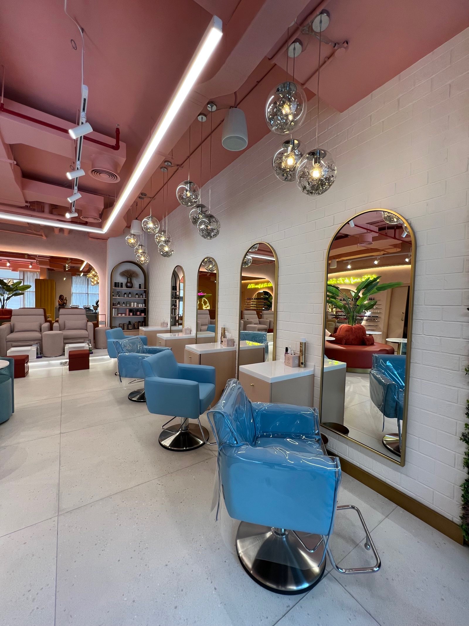 The hair section at Bellacure Al Mamoura: pink ceiling, blue styling chairs and gold-framed mirrors