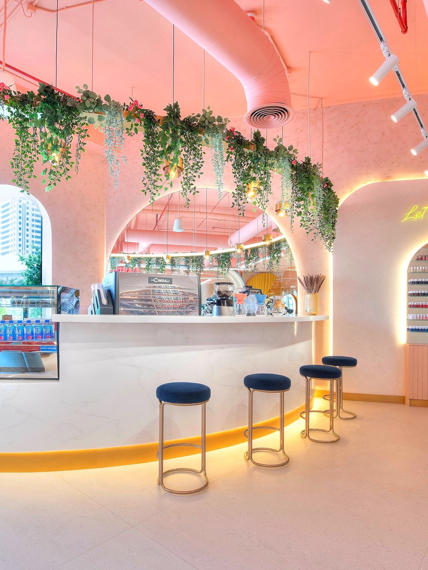 The café counter at Bellacure Sheikha Fatima Park: navy stools along a curved marble bar under trailing plants