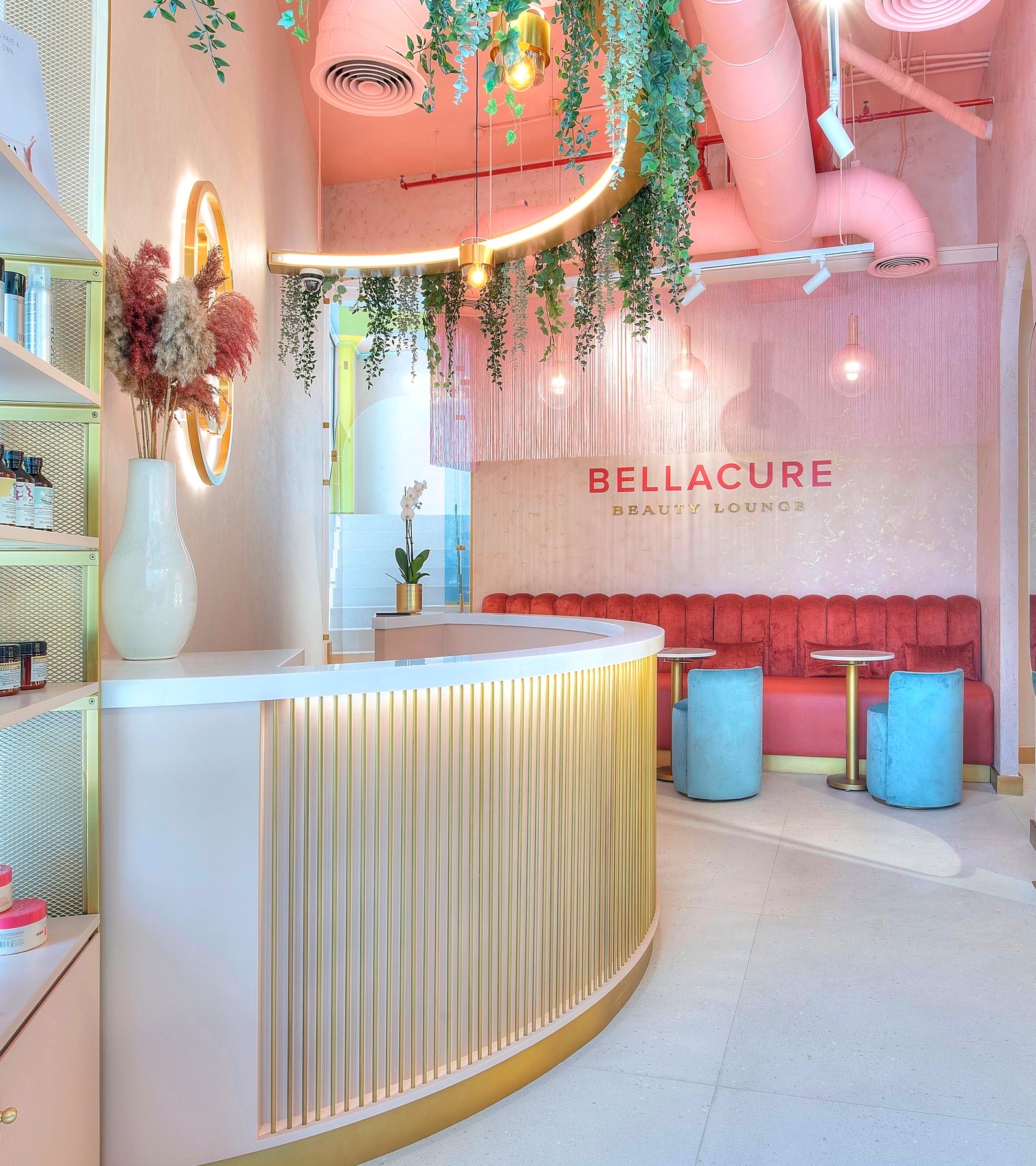 The reception at Bellacure Sheikha Fatima Park: a curved gold desk beneath trailing plants, the Bellacure Beauty Lounge sign and a red velvet banquette behind
