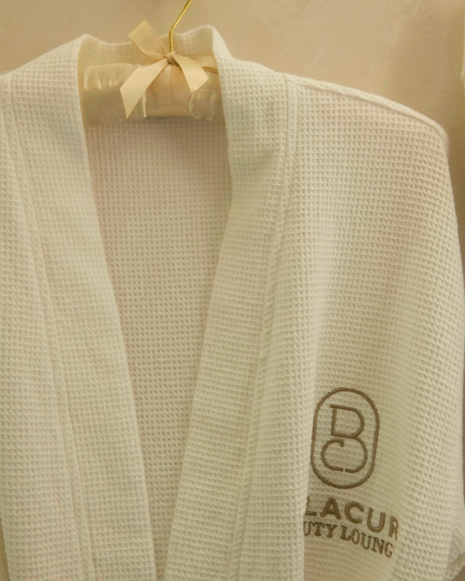 A white waffle robe with the Bellacure monogram on a gold hanger